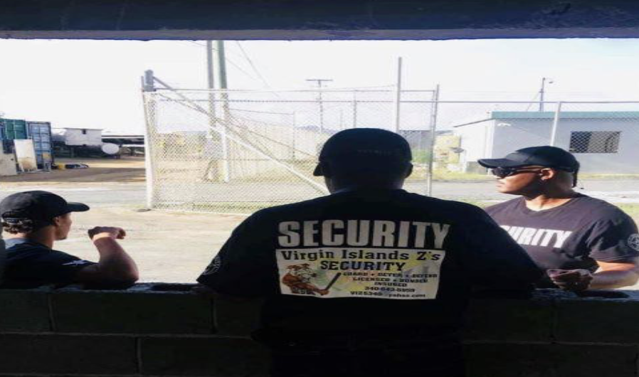 Three men in smaller hats and shirts reading "security" on them sitting at a bus stop as seen from behind them on a sunny ...